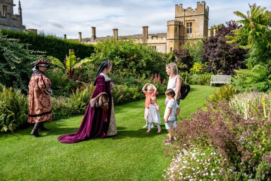 a women in tudor attire talking to a mother and two kids in mdern clothing, in a garden